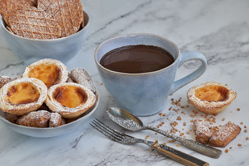 Cup of homemade chocolate accompanied by puff pastry cakes filled with custard and cookies.