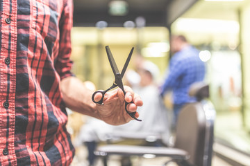 Modern man hairdresser holding sharp professional scissors at barbershop.