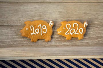 Pour feliciter 2020, gingerbread pig with year 2019 is followed by pig with 2020 sign, wooden background, Christmas stil life