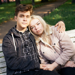 Teenagers in love sit on park bench, resting in the rays of autumn sun, looking straight ahead. Concept of teen love