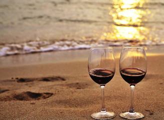 Glasses with red wine on the beach at sunset. Romantic concept.