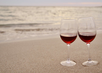 Wineglass with red wine on the beach at sunset. Romantic concept.