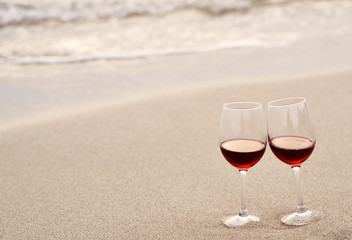 Glasses with red wine on the beach at sunset. Romantic concept.