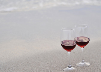 Glasses with red wine on the beach at sunset. Romantic concept.