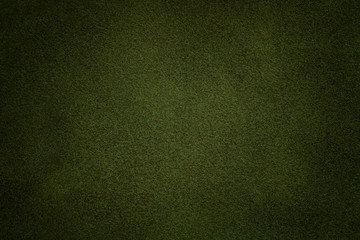 Background of dark green suede fabric closeup. Velvet matt texture of olive nubuck textile