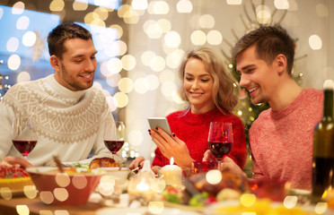 holidays and celebration concept - happy friends with smartphone having christmas dinner at home
