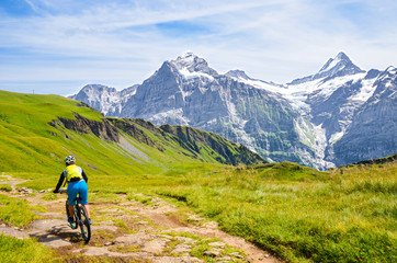 Fototapeta na wymiar Mountain biker riding downhill in the Swiss Alps. Famous mountains Jungfrau, Eiger and Monch in the background. Mountain biking, cycling in the Alps. Cyclist with a helmet. Active, outdoor sports