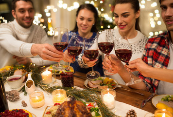 holidays and celebration concept - close up of happy friends having christmas dinner at home, drinking red wine and clinking glasses