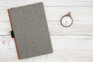 Blank gray journal with pocket watch on a weathered whitewash wood background