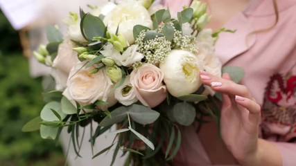 Close-up of the bride holding her wedding bouquet, she gently touches the flowers.