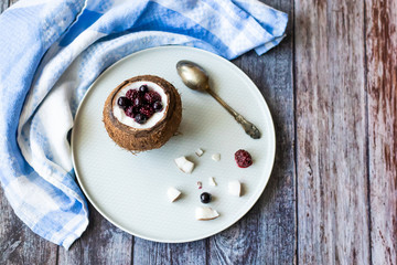 Berry dessert with yogurt in a cup of coconut on a wooden background. Blackberries, raspberries, blueberries, black currants. Blue napkin