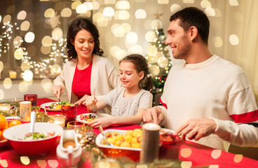 holidays, family and celebration concept - happy mother, father and little daughter having christmas dinner at home