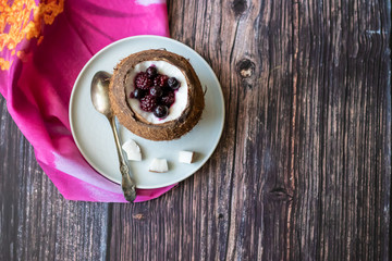 Berry dessert with yogurt in a cup of coconut on a wooden background. Blackberries, raspberries, blueberries, black currants. Pink napkin