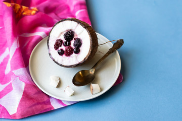 Berry dessert with yogurt in a cup of coconut on a blue background. Blackberries, raspberries, blueberries, black currants. Pink napkin