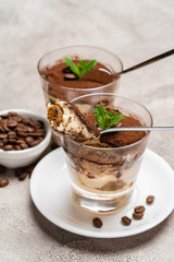 Portion of Classic tiramisu dessert in a glass cup on concrete background