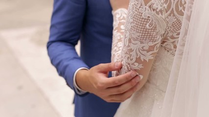 Close-up of groom hands on the bride's shoulders. Close-up of the groom embracing his bride. Rear view.