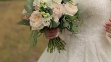 Close-up of the bride holding her wedding bouquet, she gently touches the flowers.