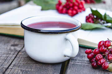 White mug or cup of hot viburnum tea on a wooden table near an open book and red viburnum berries. Source of natural vitamins. Used in folk medicine.
