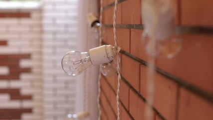 Brick wall with a garland of light bulbs. Lights Decorations for Celebratory design. Light bulbs near the brick wall. Incandescent bulbs on brick wall background in loft style.