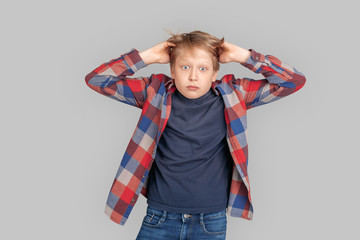 Freestyle. Young boy standing isolated on grey messing hair concerned