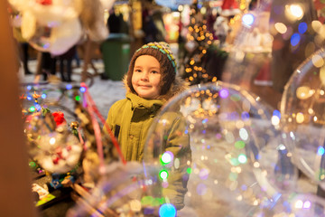 Fototapeta na wymiar holidays, childhood and people concept - happy little boy at christmas market in winter evening