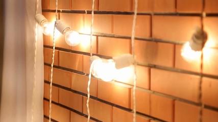 Brick wall with a garland of light bulbs. Lights Decorations for Celebratory design. Light bulbs near the brick wall. Incandescent bulbs on brick wall background in loft style.