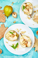 Tasty roast pears with honey and walnuts on white plates on blue background table. Top view.  Flat lay. Copy space.