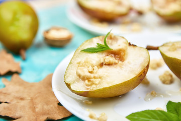 Tasty roast pears with honey and walnuts on white plates on blue background table.