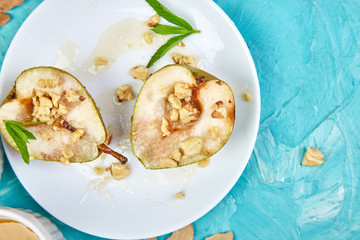 Tasty roast pears with honey and walnuts on white plates on blue background table. Top view.  Flat lay. Copy space.