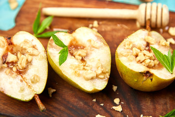 Tasty roast pears with honey and walnuts on wooden board on blue background table.