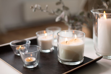 decoration, hygge and cosiness concept - burning white fragrance candles on tray on table at cozy home