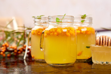 Vitaminic healthy sea buckthorn tea in small glass cups with fresh raw sea buckthorn berries, honey on black background.