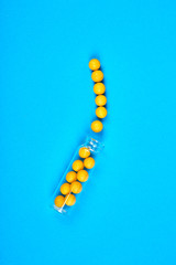 Flat lay overhead of yellow pills in glass jar on blue background with copy space for your design. Health care concept. Minimalism style template for medical blog