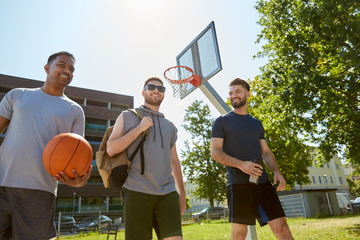 sport, leisure games and male friendship concept - group of men or friends going to play basketball outdoors