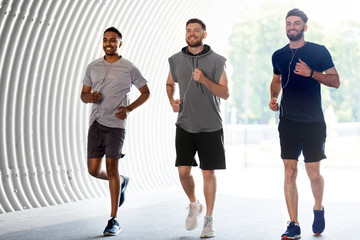 fitness, sport and healthy lifestyle concept - smiling young men or male friends with earphones running outdoors