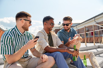 leisure, technology and people concept - happy male friends with smartphones drinking beer and talking on street in summer