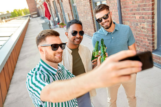 leisure, technology and people concept - happy male friends taking selfie by smartphone and drinking beer at rooftop party in summer city,