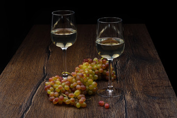 Two glasses of white wine and a bunch of grapes on wooden table.