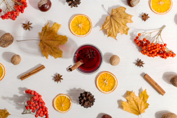 A cup of mulled wine with spices, dry leaves and oranges on the table. Autumn mood, a method to keep warm in the cold, morning light, flat lay.