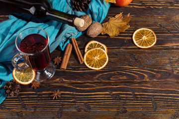 Cup of mulled wine with spices, bottle, scarf, dry leaves and oranges on a wooden table. Autumn mood, method to keep warm in the cold, copy space.