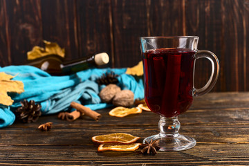 Naklejka na ściany i meble Cup of mulled wine with spices, bottle, scarf, dry leaves and oranges on a wooden table. Autumn mood, method to keep warm in the cold, copy space.