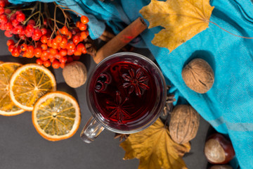 Cup of mulled wine with spices, a scarf, dry leaves and oranges on a stone table. Autumn mood, a method to keep warm in the cold.