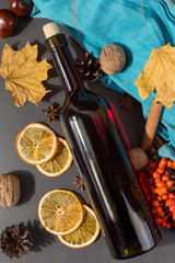 A bottle of mulled wine with spices, a scarf, dry leaves and oranges on a stone table. Autumn mood, a method to keep warm in the cold.