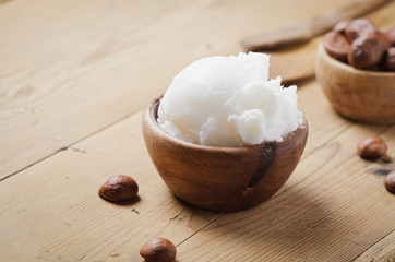 Shea butter in wooden bowl with nuts on old rustic table. Free text space.