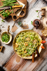 overhead shot of tasty homemade italian pasta with grilled shrimps, pesto sauce, parmesan cheese, fresh basil in ceramic bowl on wooden rustic table