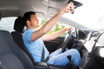 transport, vehicle and driving concept - man or car driver adjusting mirror in summer