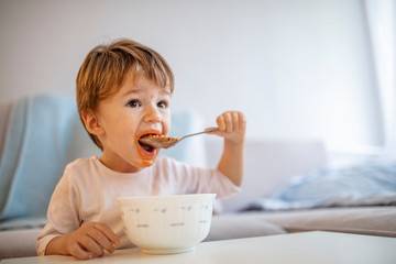 Cute child eating healthy food with with the left hand at home. Cute child little boy eats healthy...