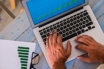 close up of hands writing and working with laptop at the office on a blue wood table with stadistics and graphs