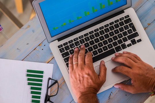 close up of hands writing and working with laptop at the office on a blue wood table with stadistics and graphs