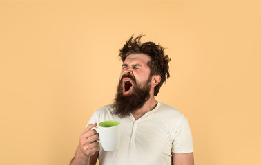 Tired guy hold coffee mug. Man with sleepy face try to awake with cup of coffee. Yawning man hold...